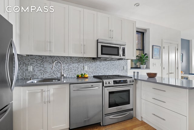 kitchen with dark countertops, a peninsula, stainless steel appliances, white cabinetry, and a sink