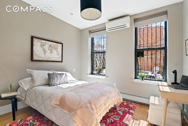 bedroom with baseboard heating, a wall mounted AC, baseboards, and wood finished floors