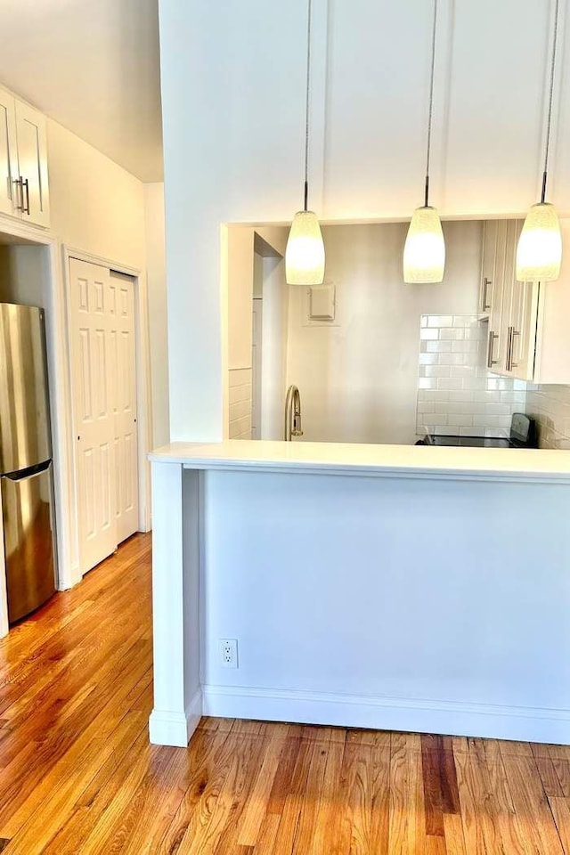 kitchen with light wood-style flooring, decorative light fixtures, backsplash, freestanding refrigerator, and light countertops