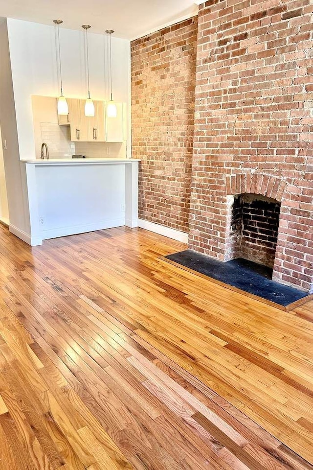 unfurnished living room featuring brick wall, a fireplace, baseboards, and wood-type flooring