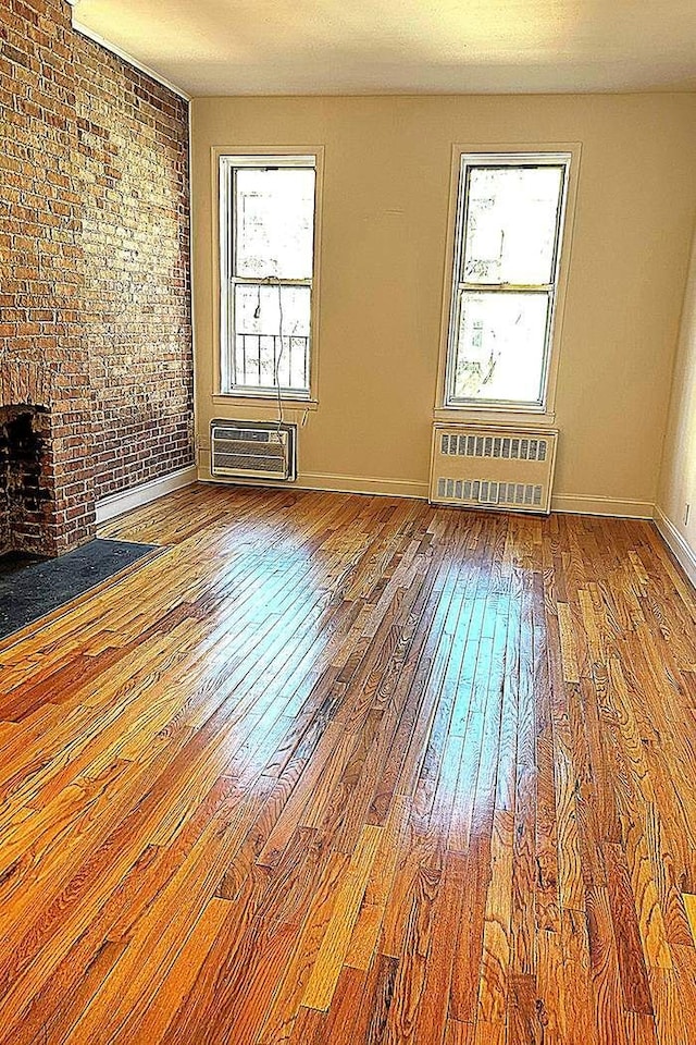 empty room featuring a wall unit AC, hardwood / wood-style flooring, radiator heating unit, and a wealth of natural light