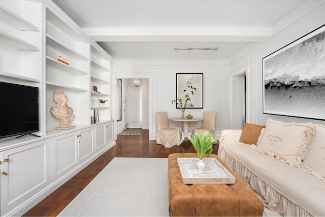 living area featuring built in shelves, dark wood finished floors, rail lighting, and a decorative wall