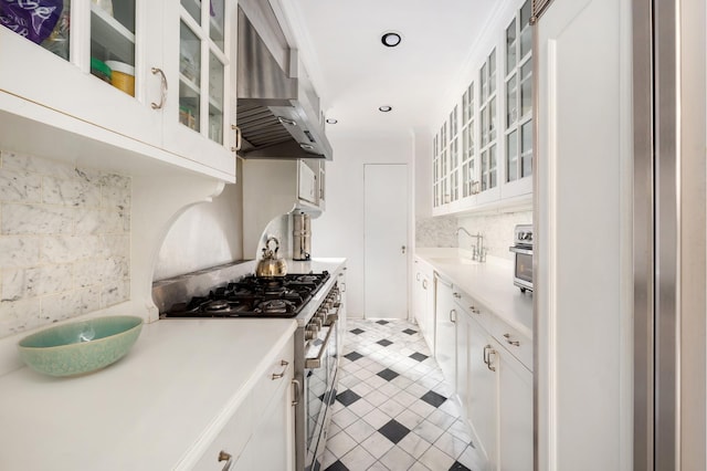 kitchen with decorative backsplash, light countertops, wall chimney range hood, and stainless steel gas stove