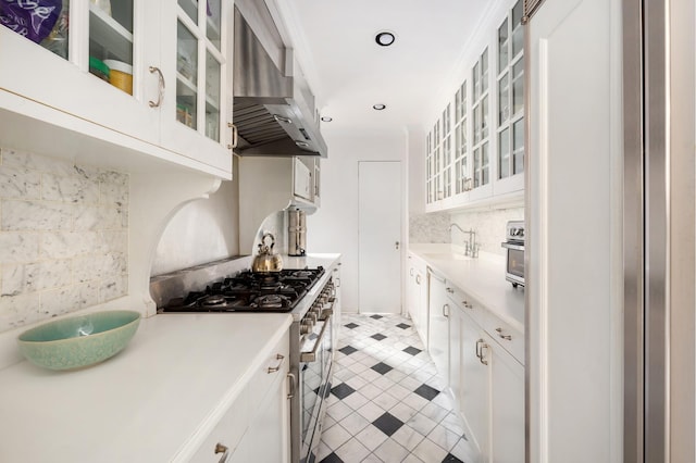 kitchen with light countertops, wall chimney exhaust hood, backsplash, and stainless steel gas range