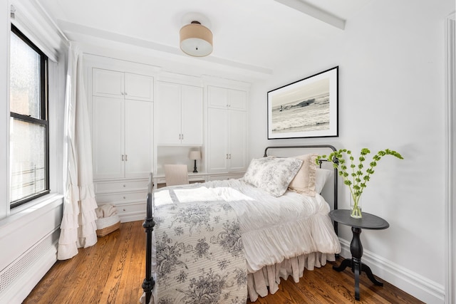 bedroom with a baseboard heating unit, wood finished floors, and baseboards