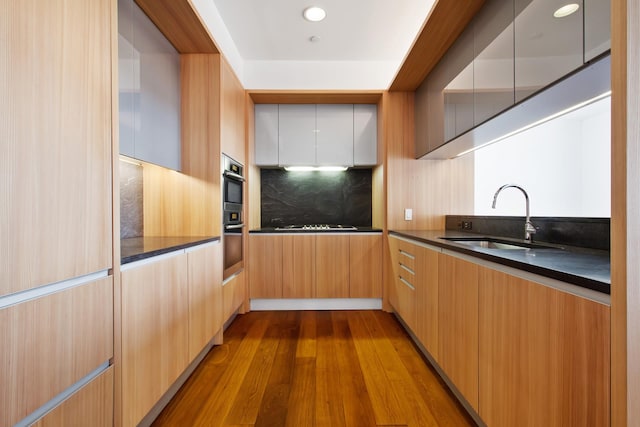 kitchen with modern cabinets, a sink, tasteful backsplash, dark countertops, and dark wood-style floors