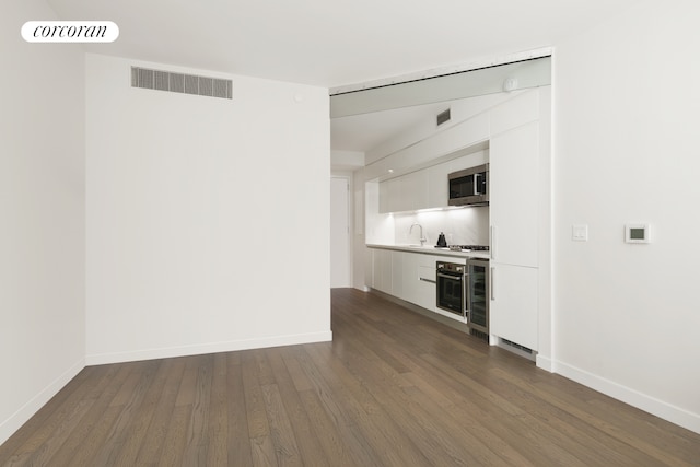 interior space featuring oven, visible vents, stainless steel microwave, white cabinets, and dark wood-style flooring