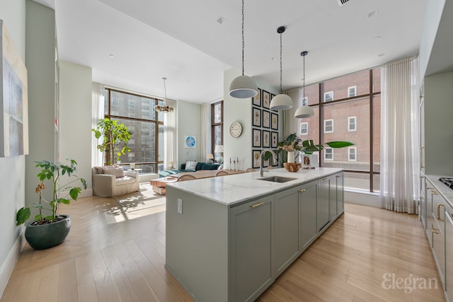kitchen with an island with sink, gray cabinetry, a sink, and a wall of windows