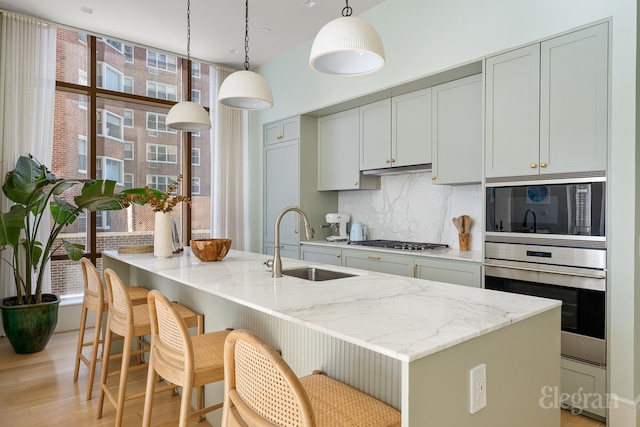 kitchen featuring a sink, light stone counters, backsplash, and appliances with stainless steel finishes