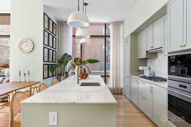 kitchen featuring a center island with sink, a sink, backsplash, stainless steel appliances, and light wood-style floors