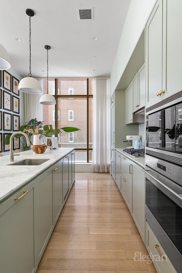 kitchen featuring visible vents, light stone countertops, decorative light fixtures, light wood-type flooring, and a sink