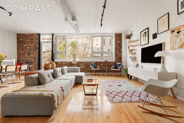 living room with wood-type flooring, brick wall, and track lighting