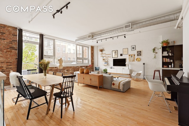 dining space with visible vents, light wood-style flooring, brick wall, and rail lighting