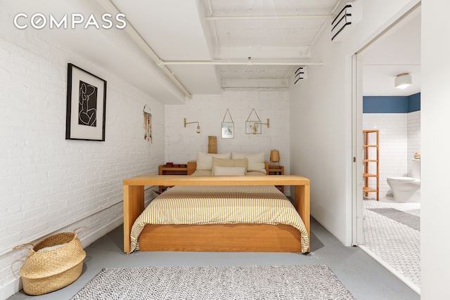 bedroom featuring connected bathroom, concrete floors, and brick wall