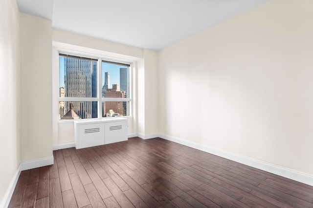 empty room featuring dark wood finished floors, a view of city, and baseboards