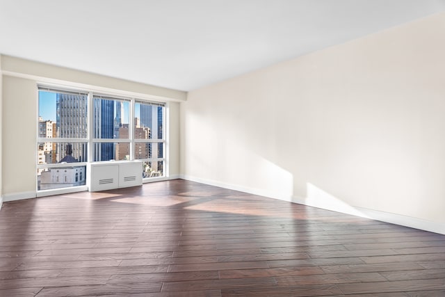 unfurnished room with a view of city, wood finished floors, and baseboards