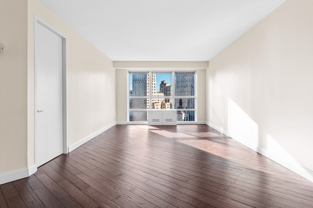 unfurnished room with hardwood / wood-style floors, a view of city, and baseboards