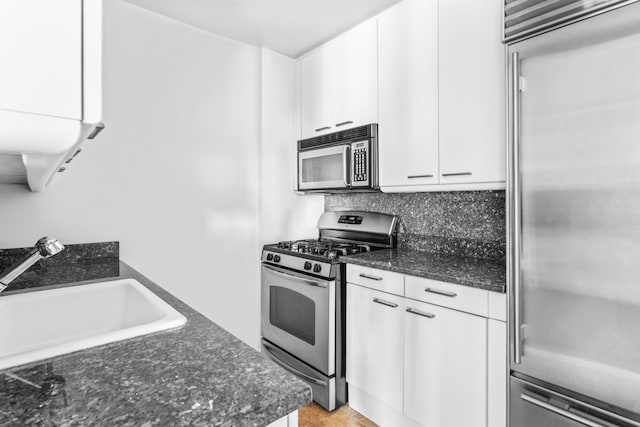 kitchen with a sink, white cabinetry, dark stone counters, appliances with stainless steel finishes, and decorative backsplash