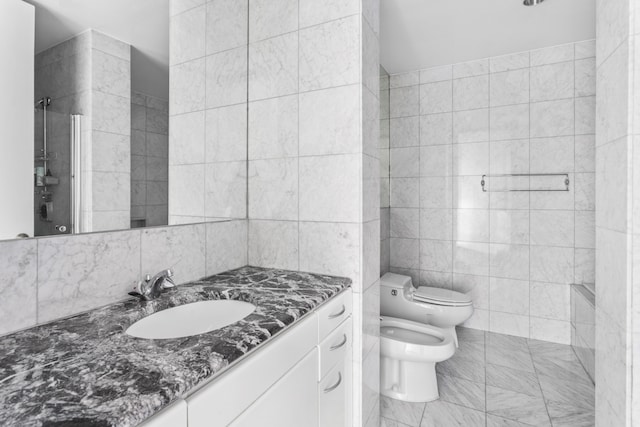 bathroom with a bidet, toilet, tile walls, and vanity