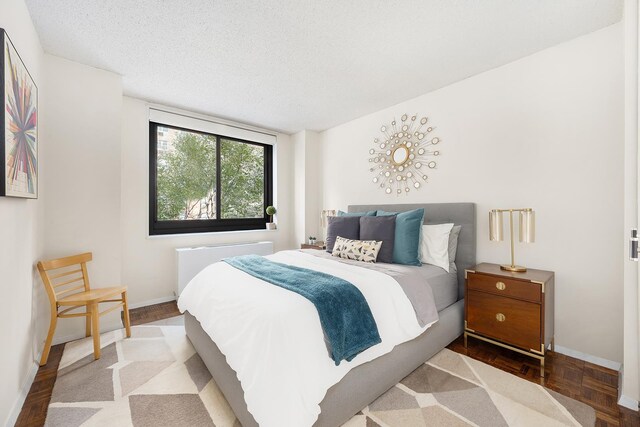347 W 57th St Unit 3B, New York City, NY 10019 - bedroom featuring radiator heating unit, baseboards, wood finished floors, and a textured ceiling