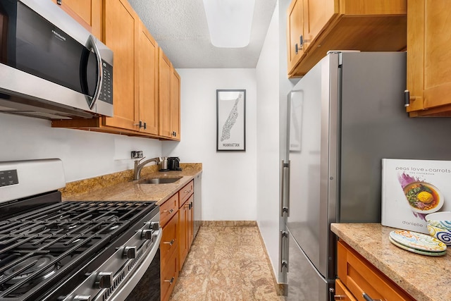 kitchen featuring a sink, light stone counters, a textured ceiling, and appliances with stainless steel finishes