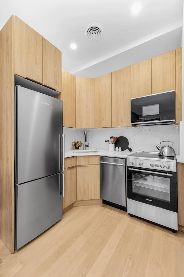 kitchen with light brown cabinets, visible vents, appliances with stainless steel finishes, and a sink