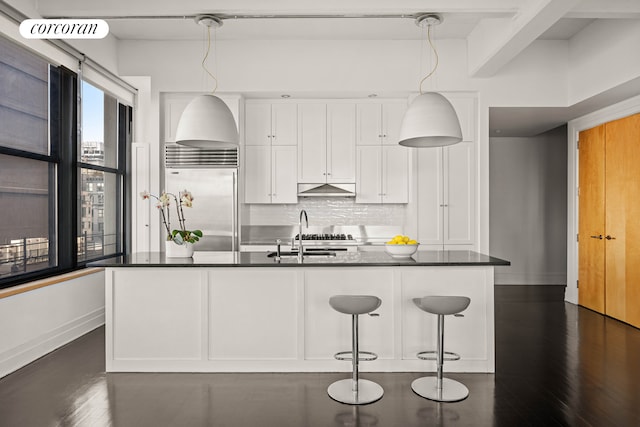 kitchen with under cabinet range hood, white cabinets, dark countertops, and stainless steel built in fridge