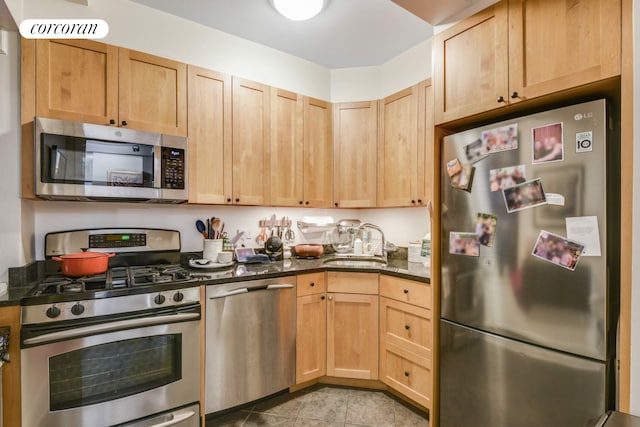 kitchen with dark stone counters, a sink, appliances with stainless steel finishes, and light brown cabinets