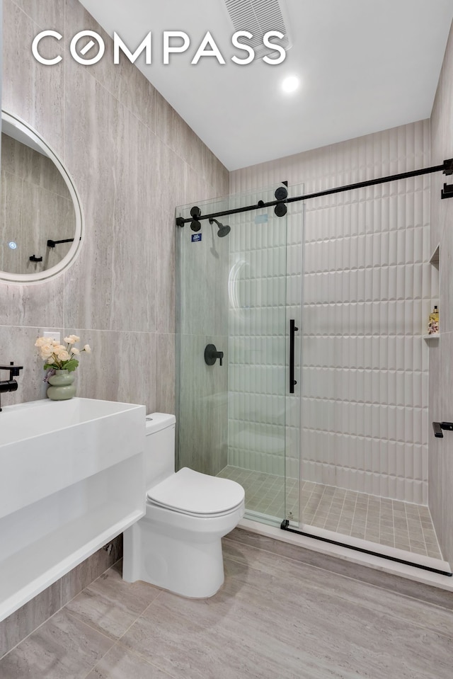 bathroom featuring a stall shower, toilet, and tile walls