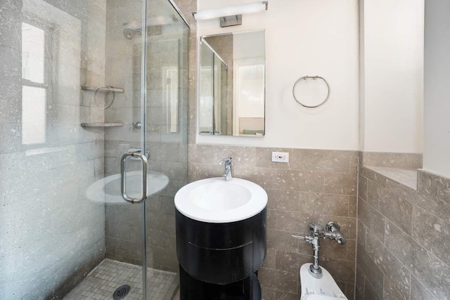 full bath with vanity, a shower stall, tile walls, and wainscoting