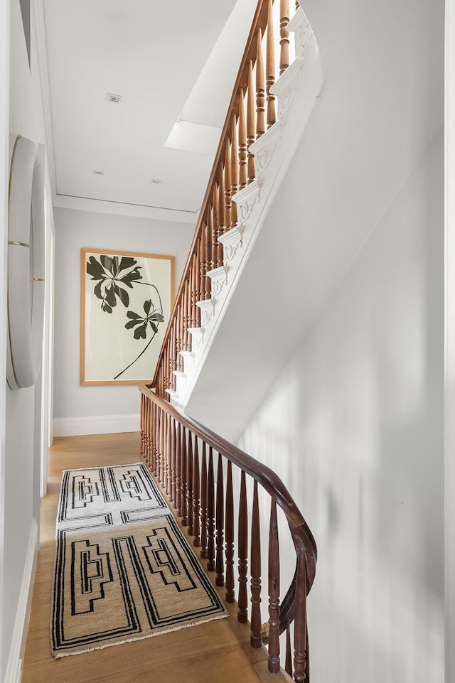 staircase with wood finished floors, baseboards, and ornamental molding