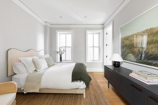 bedroom featuring baseboards, crown molding, and light wood finished floors