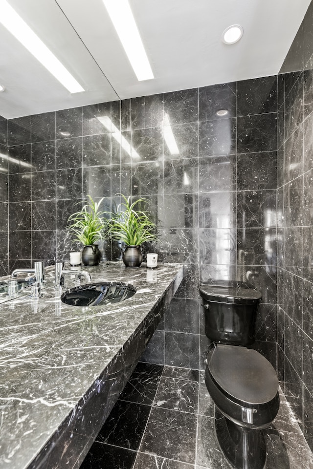 bathroom featuring toilet, recessed lighting, marble finish floor, tile walls, and a sink