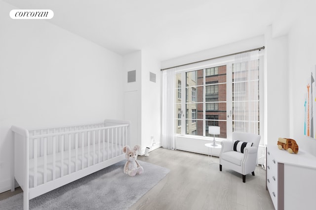 bedroom with visible vents, a nursery area, and wood finished floors