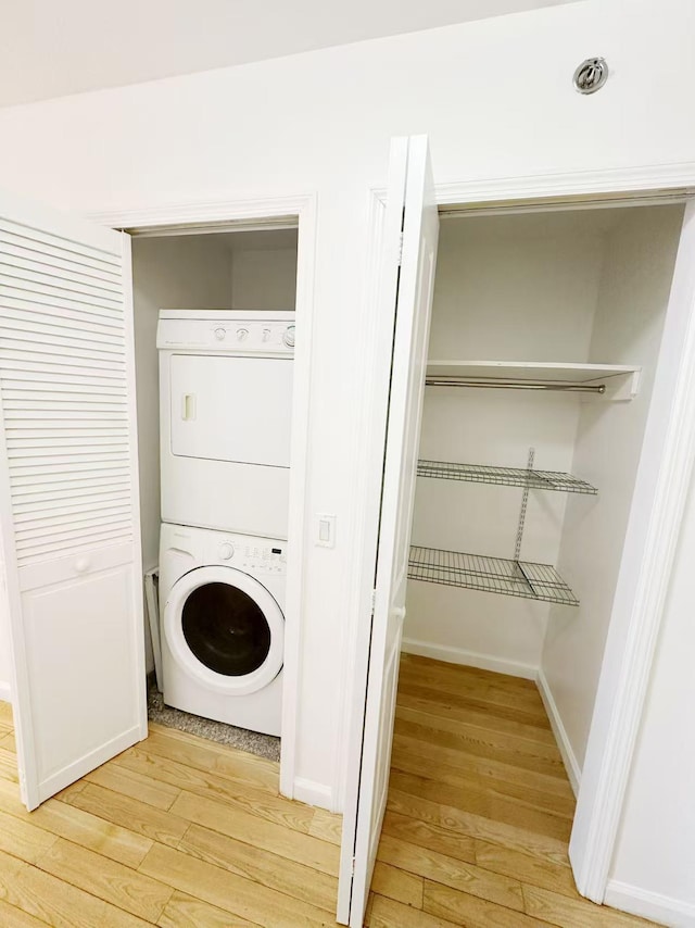 washroom featuring baseboards, stacked washer and clothes dryer, light wood-style flooring, and laundry area