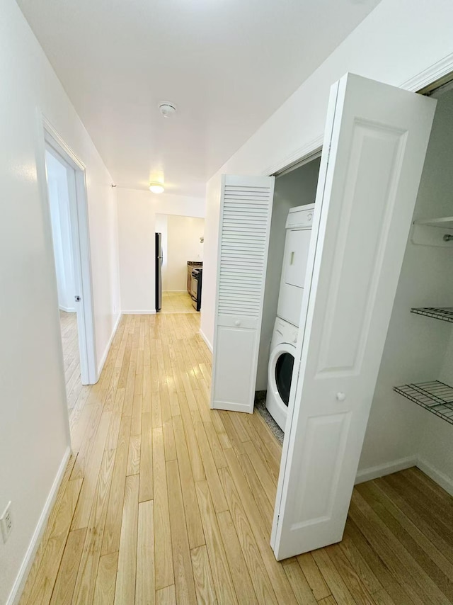 corridor with baseboards, stacked washing maching and dryer, and light wood-style floors