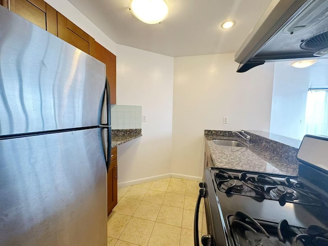 kitchen with range with gas stovetop, decorative backsplash, freestanding refrigerator, brown cabinetry, and a sink