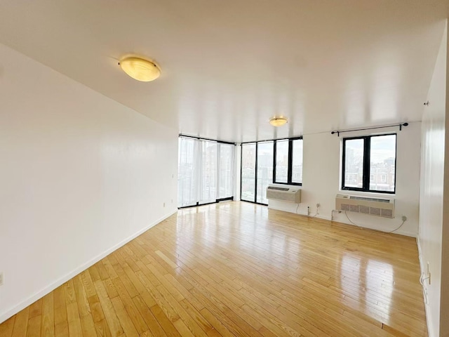 unfurnished room featuring floor to ceiling windows, light wood finished floors, baseboards, and a wall mounted air conditioner