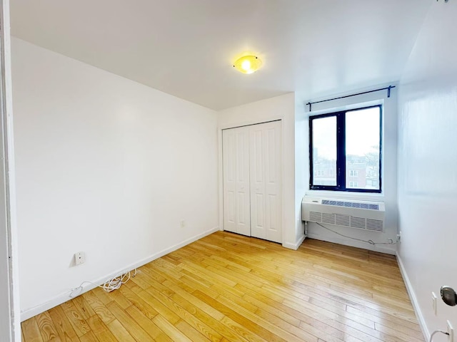 unfurnished bedroom with a closet, baseboards, an AC wall unit, and light wood finished floors