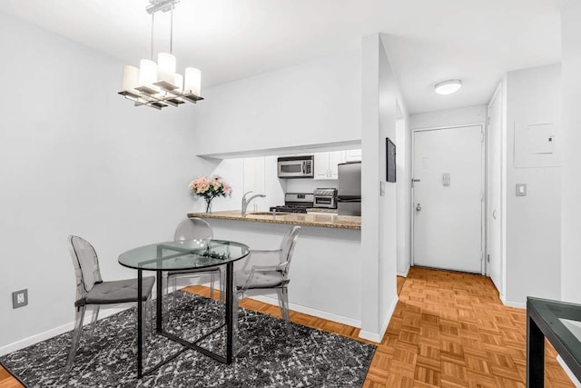 kitchen featuring a toaster, appliances with stainless steel finishes, a peninsula, hanging light fixtures, and white cabinetry