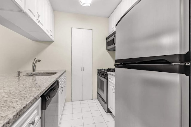 kitchen featuring light tile patterned floors, light stone counters, appliances with stainless steel finishes, white cabinetry, and a sink