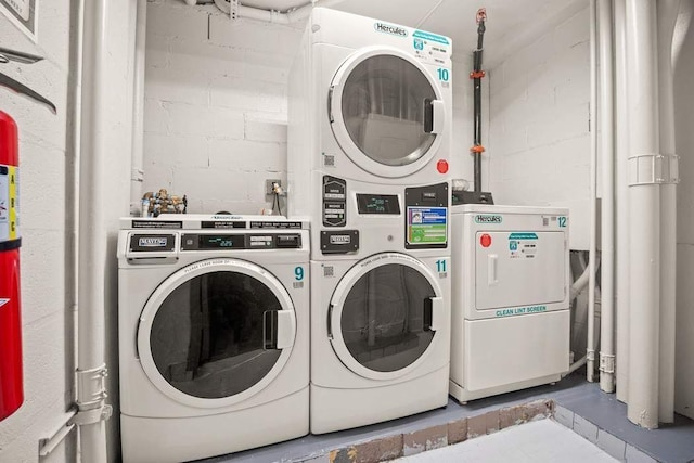 common laundry area featuring separate washer and dryer, concrete block wall, and stacked washing maching and dryer