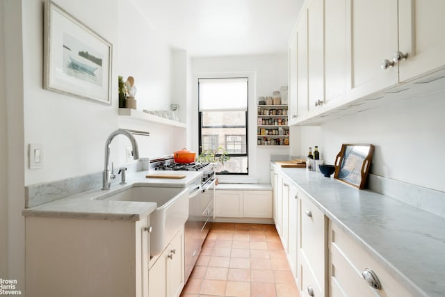 kitchen with gas stove, light tile patterned floors, white cabinetry, open shelves, and a sink
