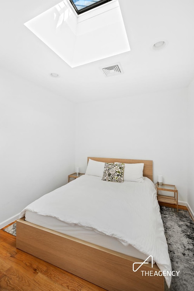 bedroom featuring a skylight, wood finished floors, visible vents, and baseboards