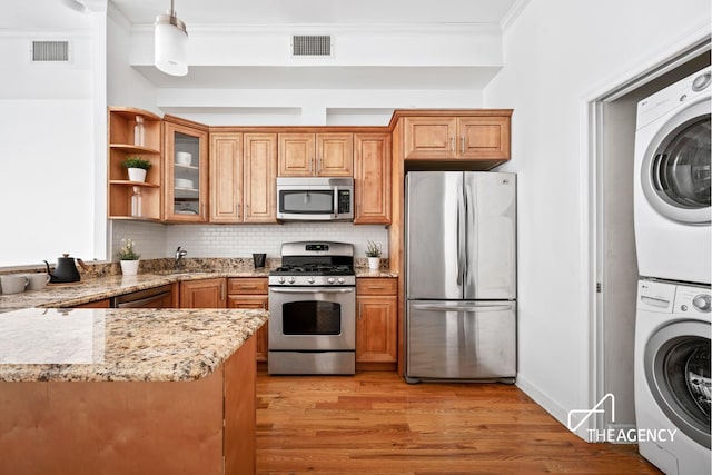 146 W 136th St, New York City, NY 10030 - kitchen featuring appliances with stainless steel finishes, stacked washer and clothes dryer, light stone counters, brown cabinets, and ornamental molding