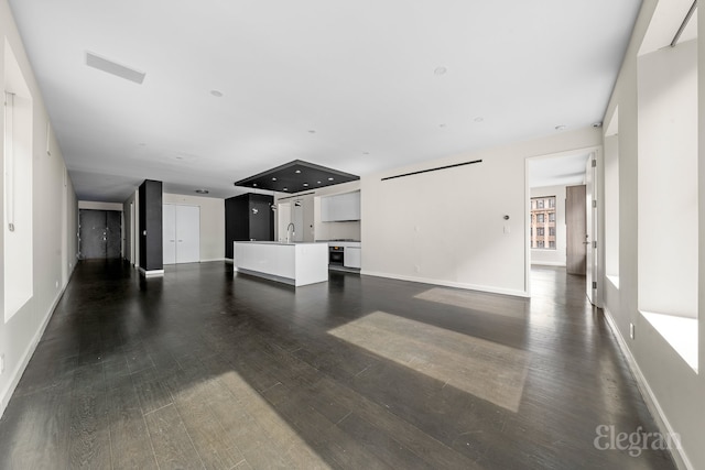 unfurnished living room with a sink, baseboards, visible vents, and dark wood-style flooring