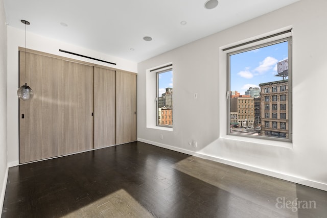 unfurnished bedroom with a view of city, wood finished floors, and baseboards