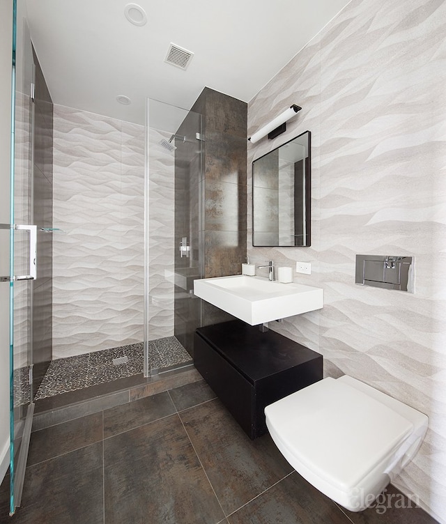 full bathroom featuring a tile shower, visible vents, tile walls, and a sink