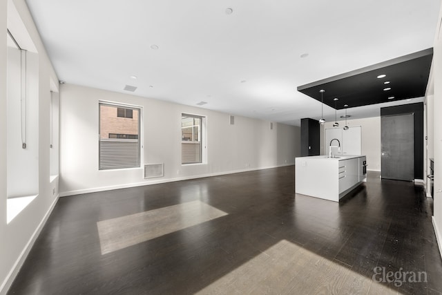 unfurnished living room with dark wood finished floors, visible vents, baseboards, and a sink