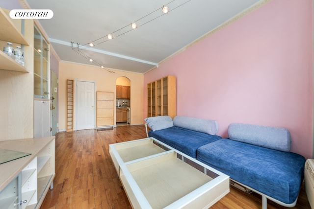 living area featuring visible vents, arched walkways, rail lighting, light wood-style floors, and crown molding